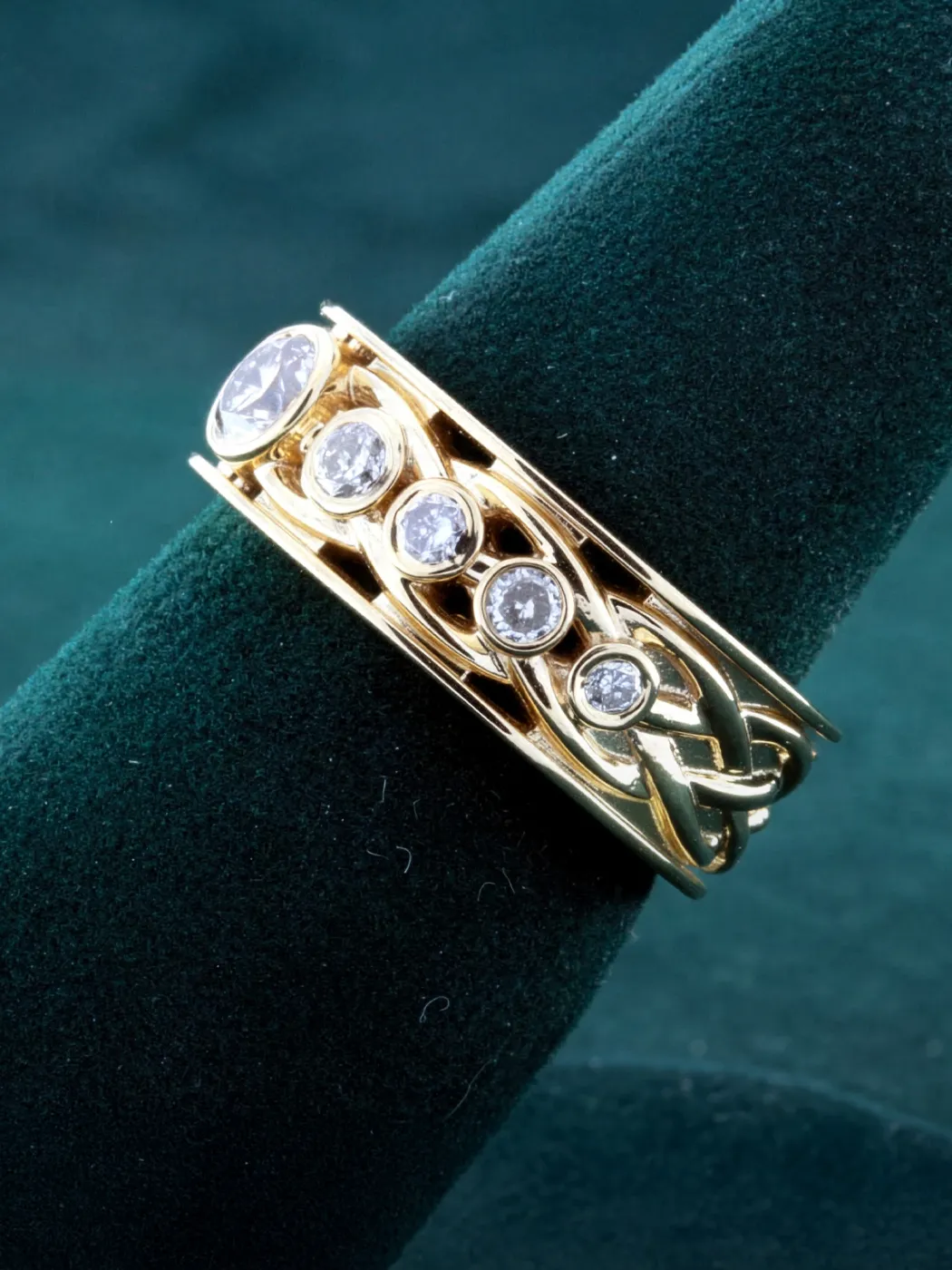 Gold diamond ring with intricate design featuring multiple sparkling stones, displayed on a green velvet stand.