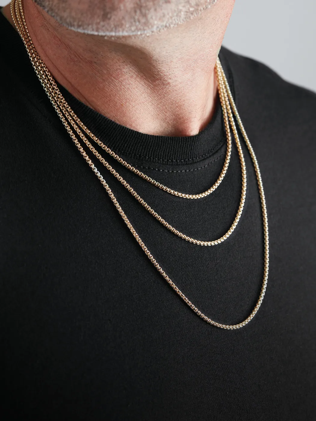 Three layered chains in gold and silver worn by a man in a black shirt.