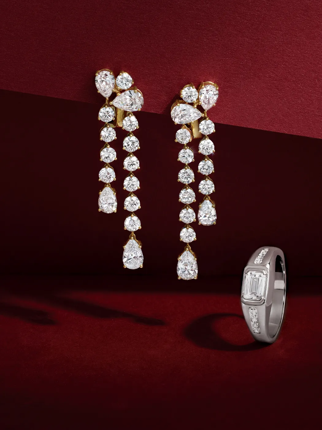 Elegant diamond drop earrings and a sleek ring on a rich burgundy background.