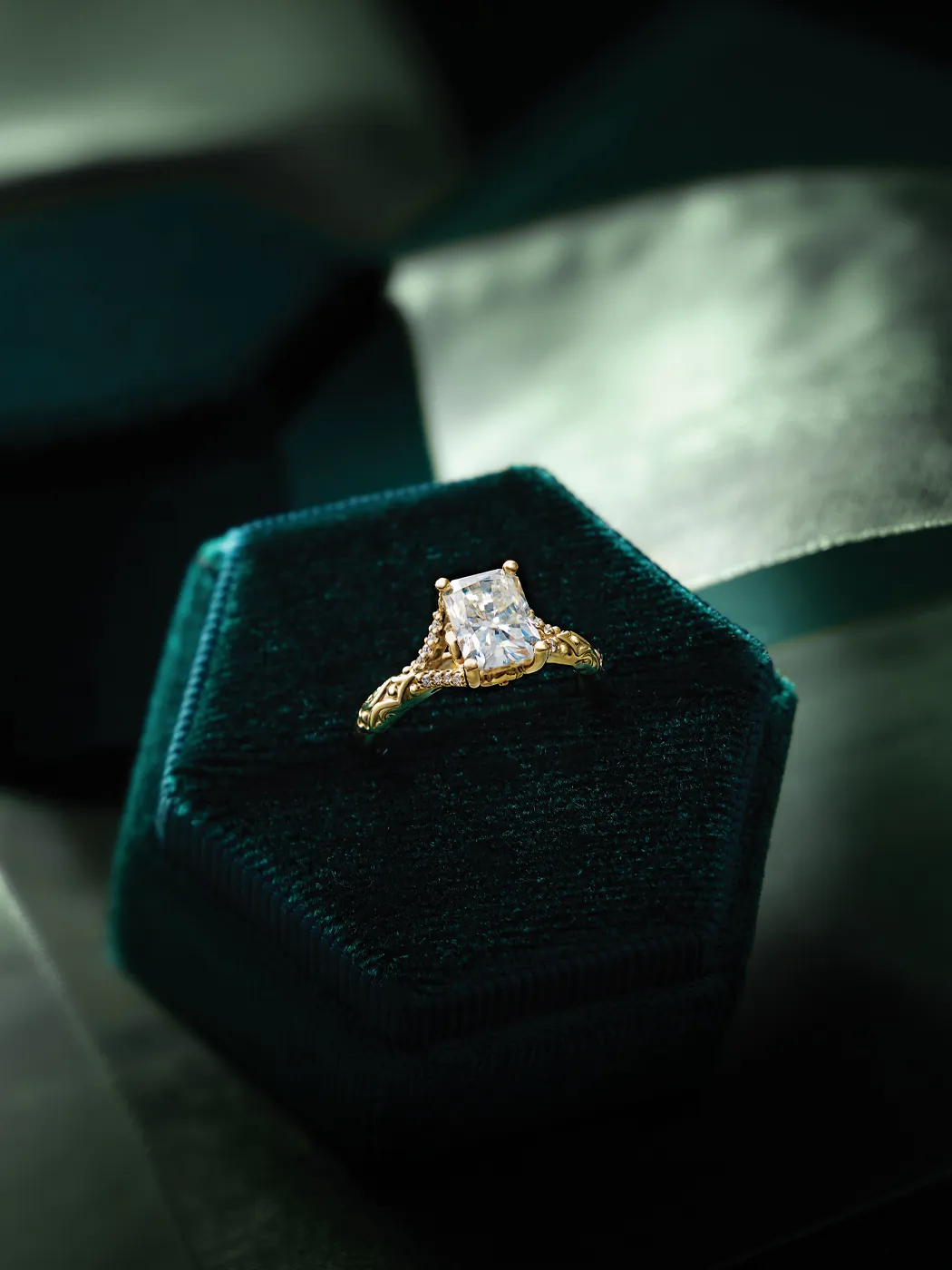 Elegant gold engagement ring with a large diamond, displayed on a dark green velvet box.
