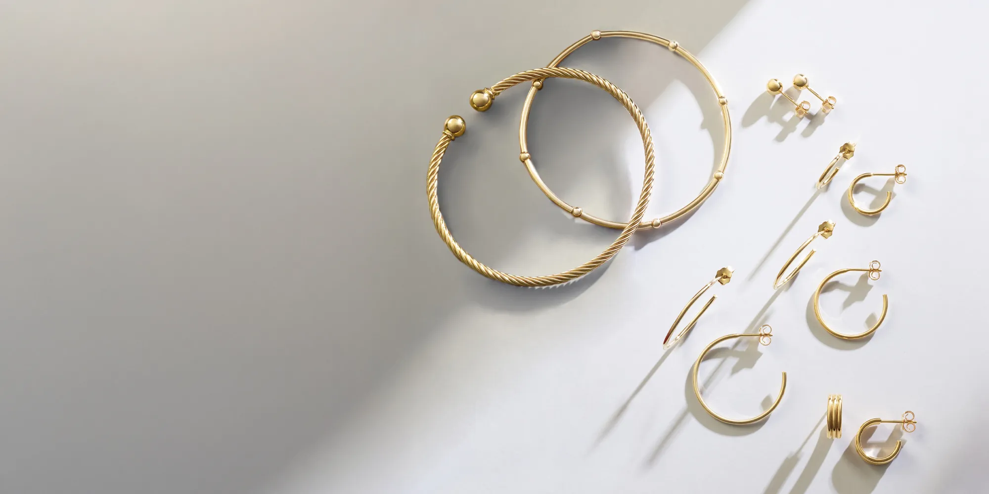 Gold earrings and hoops arranged artistically on a light background.
