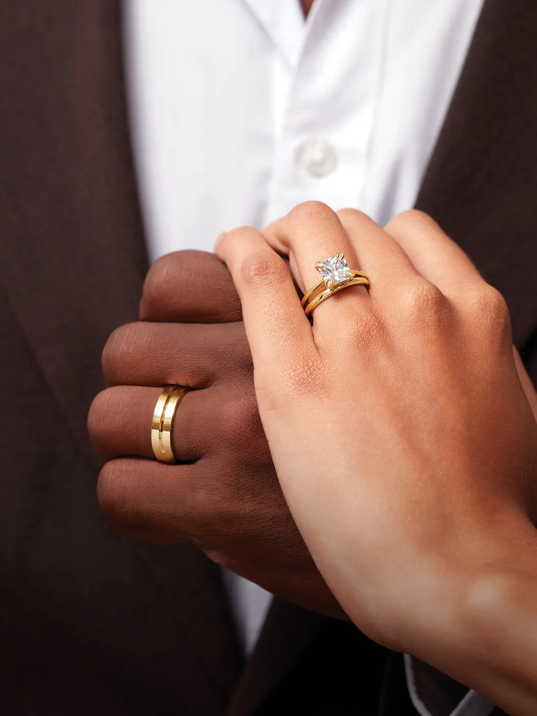 A couple holding hands, showcasing a diamond engagement ring and matching wedding bands.