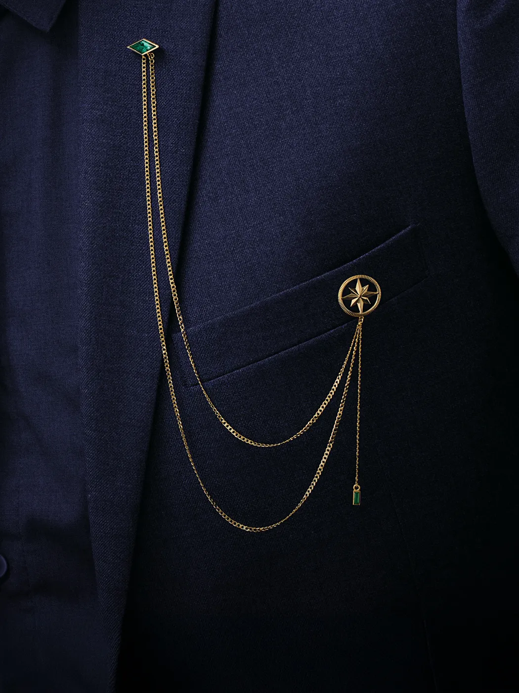 Gold chain accessories with emerald accents on a navy blazer pocket. Shop accessories at Rich Custom Jewelry, Las Vegas.