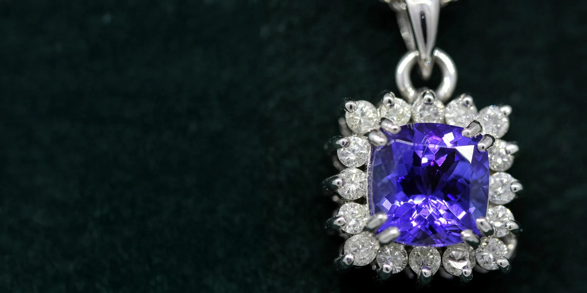 Purple gemstone pendant surrounded by diamonds on a dark background. 
