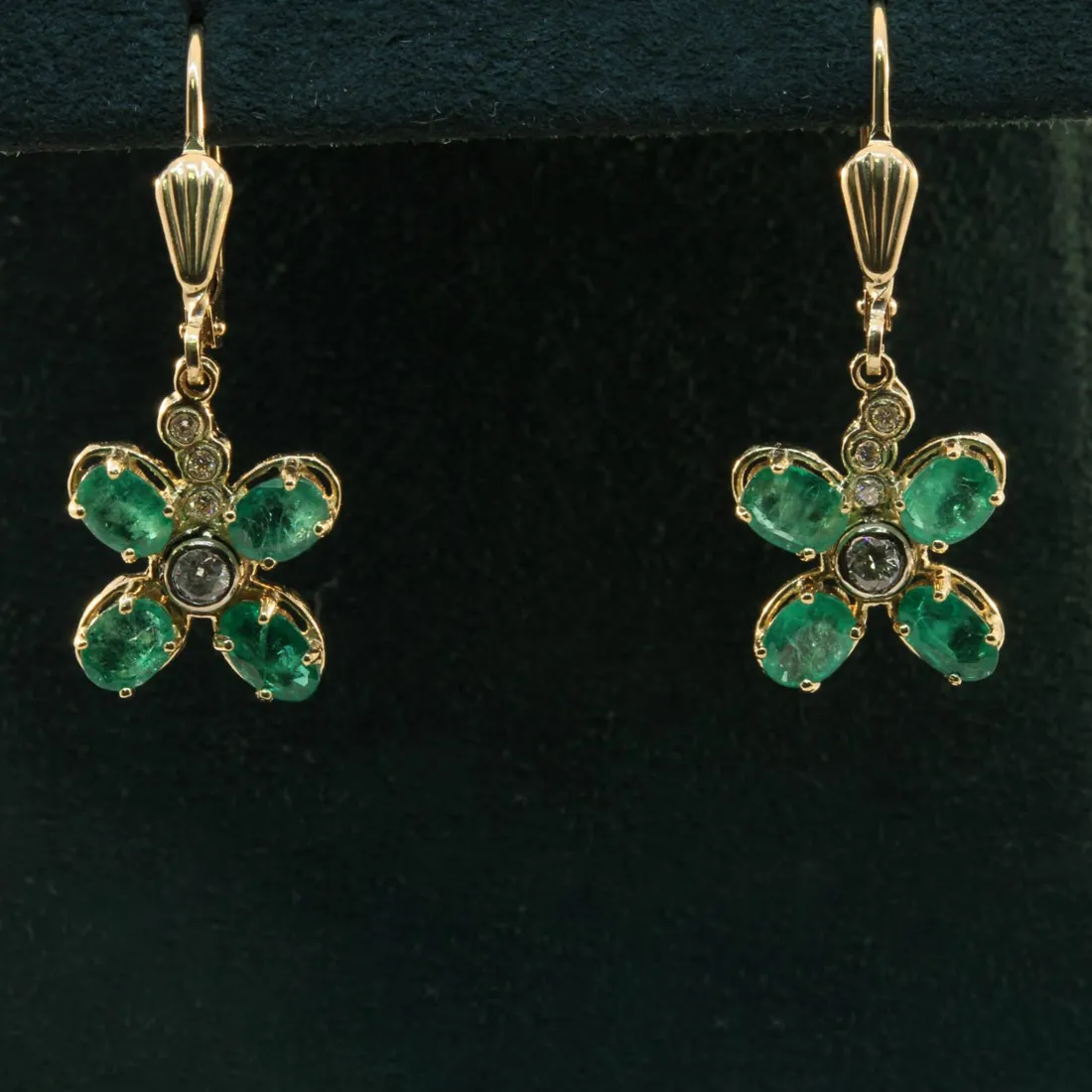 Emerald flower earrings with gold accents and diamond details, displayed on a dark background.