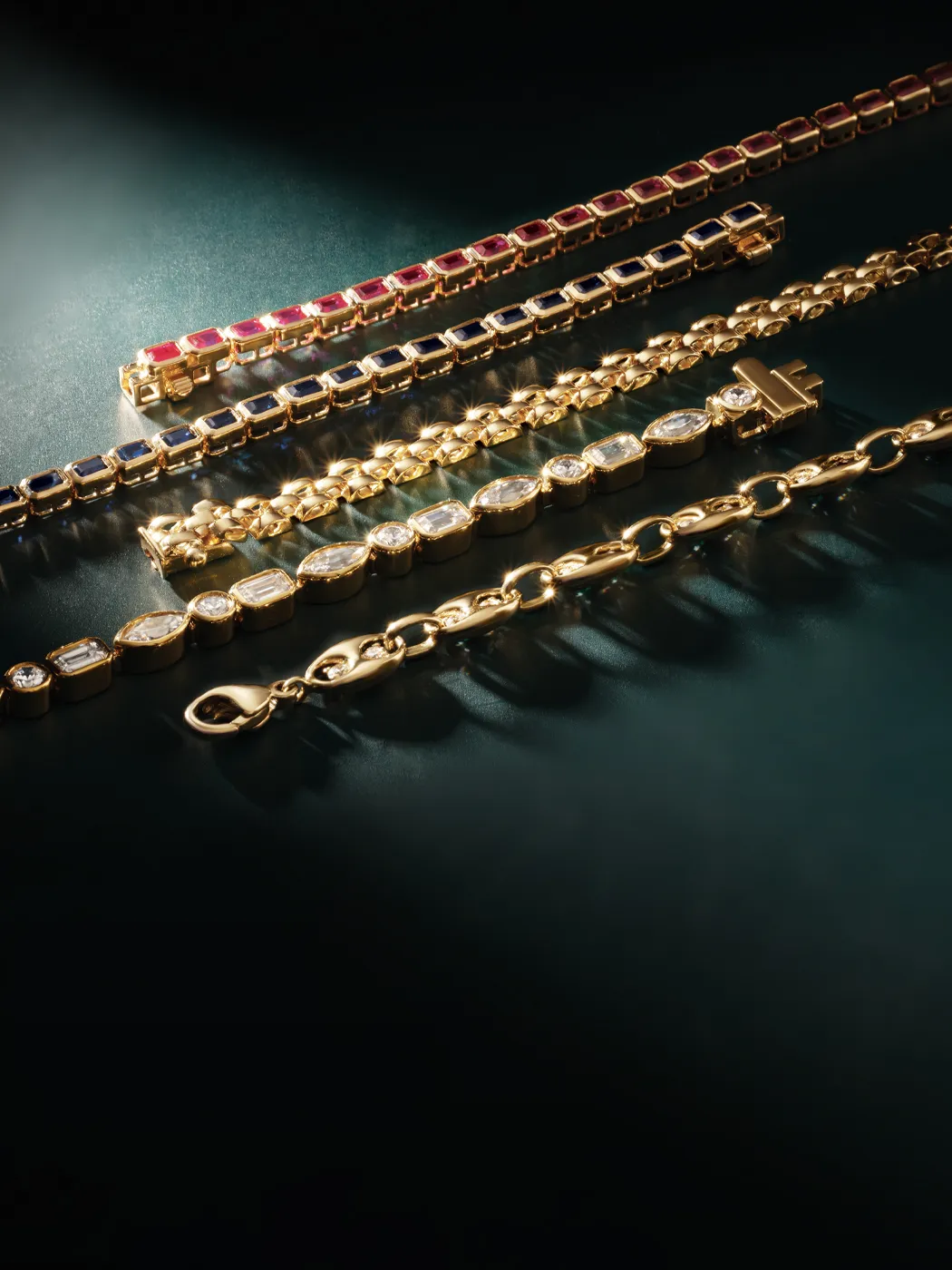 Elegant collection of gold bracelets with colorful gemstones, displayed on a dark surface.