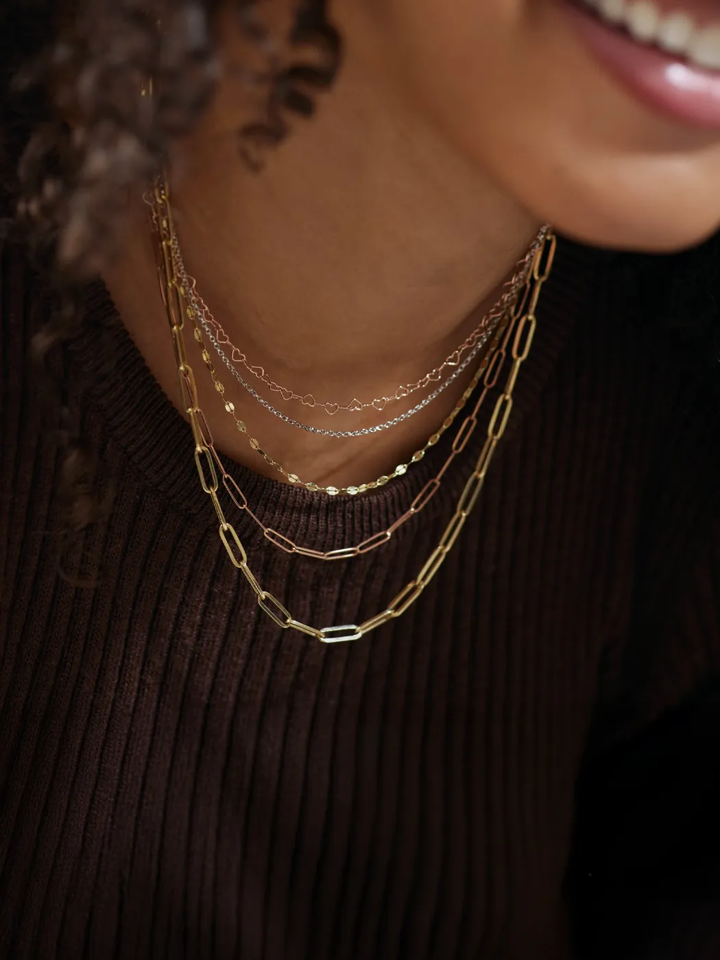Layered gold and silver chains worn by a woman, showcasing delicate designs and textures.