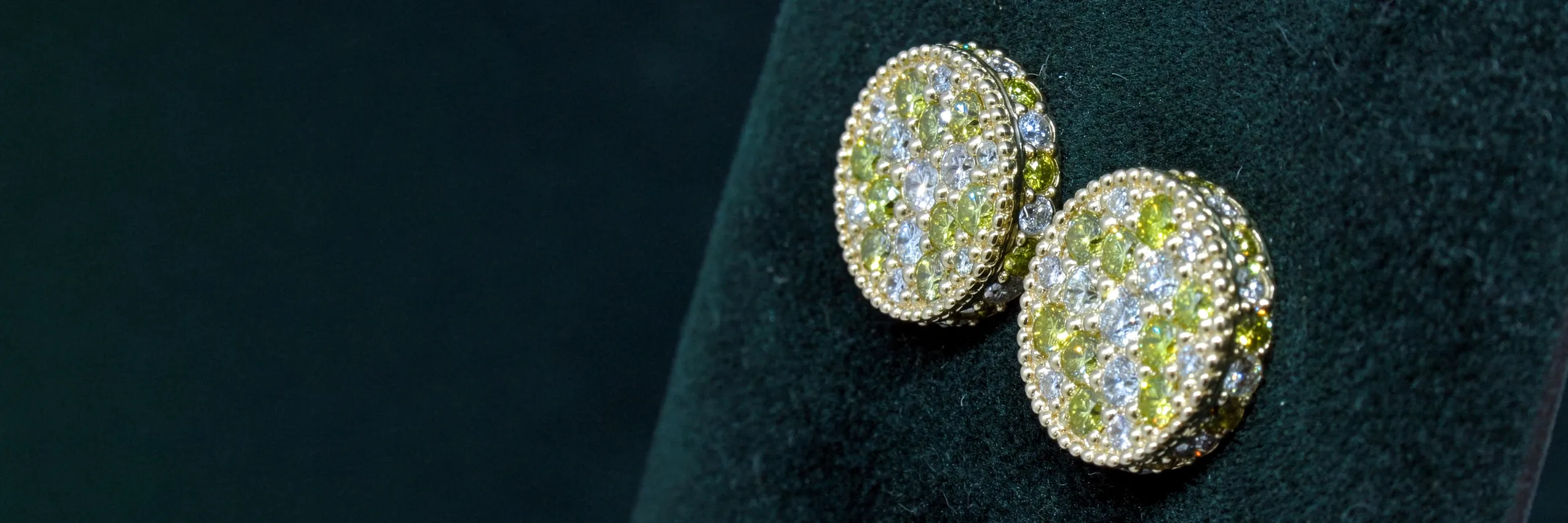 Elegant gold and gemstone earrings featuring green and clear stones, displayed on a dark velvet background.