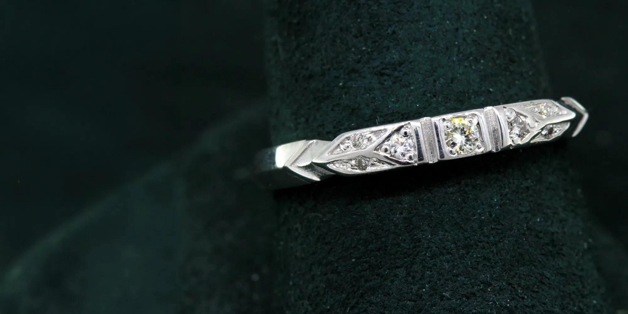 Elegant silver ring with three sparkling diamonds, displayed on a dark green velvet background.