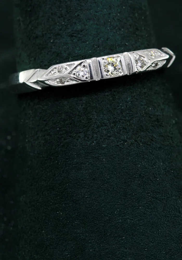 Elegant silver ring with three sparkling diamonds, displayed on a dark green velvet background.
