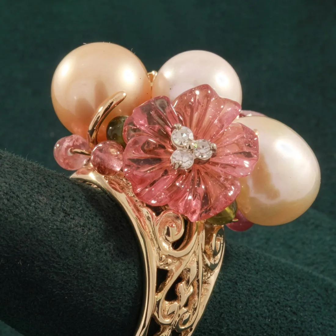 Gold ring adorned with pink flower, pearls, and gemstones, showcasing intricate design.