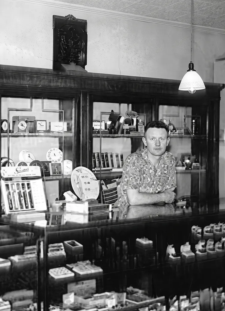 Man in a vintage store with display cases of clocks and products.