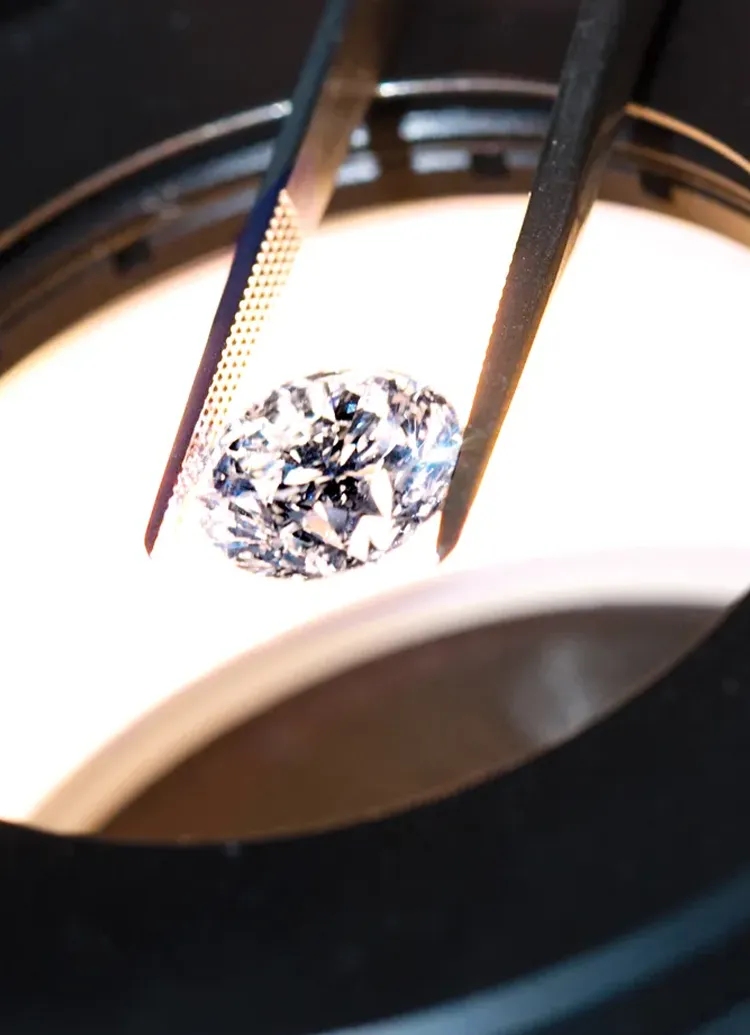 A diamond held by tweezers under magnifying light at Rinehart Jewelry Co.