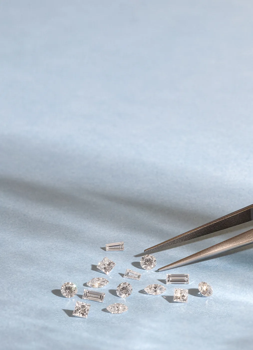 Various cut diamonds on a light blue surface with tweezers.