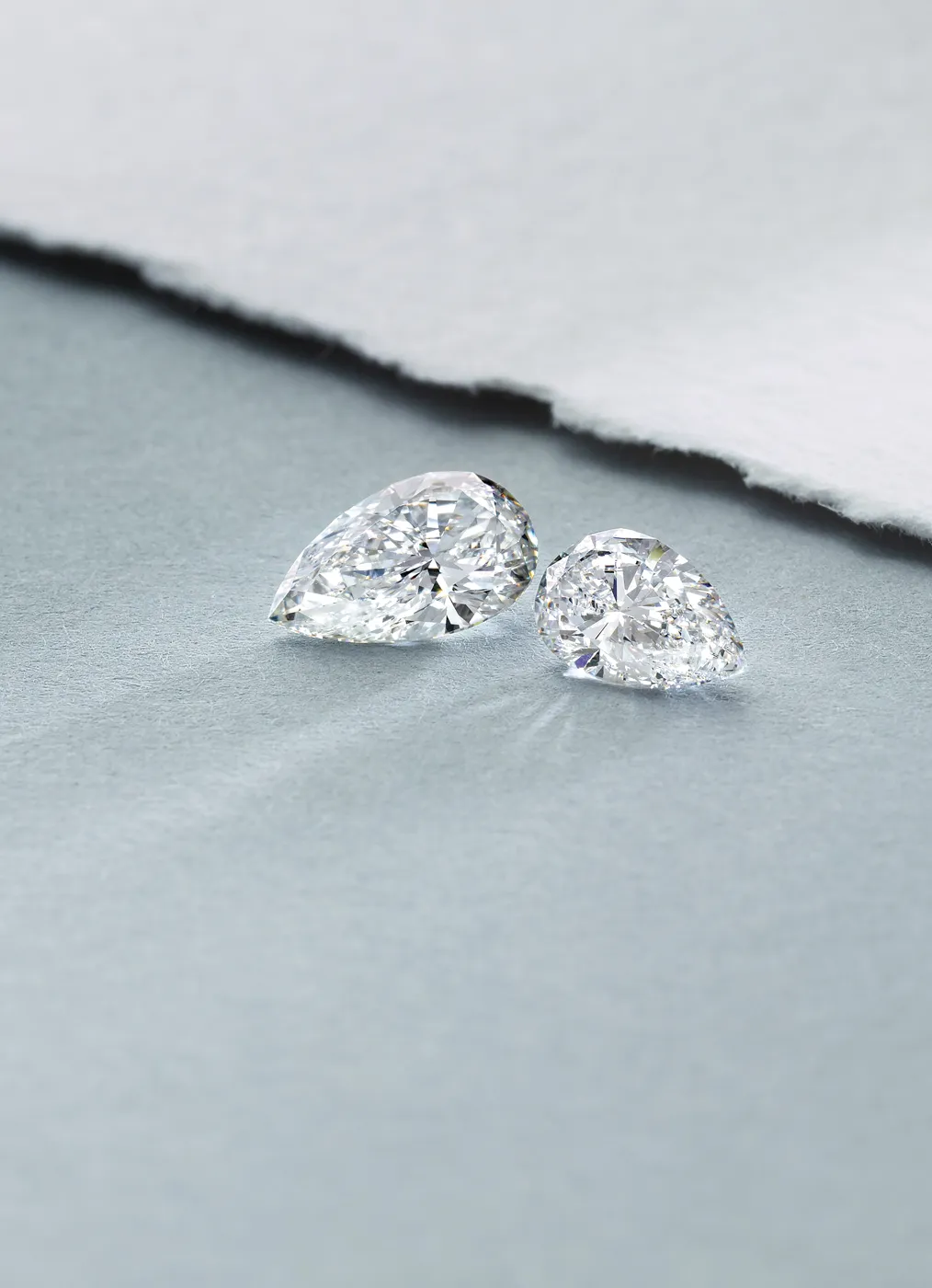 Two pear-shaped diamonds on a textured surface, showcasing their brilliance and cut.