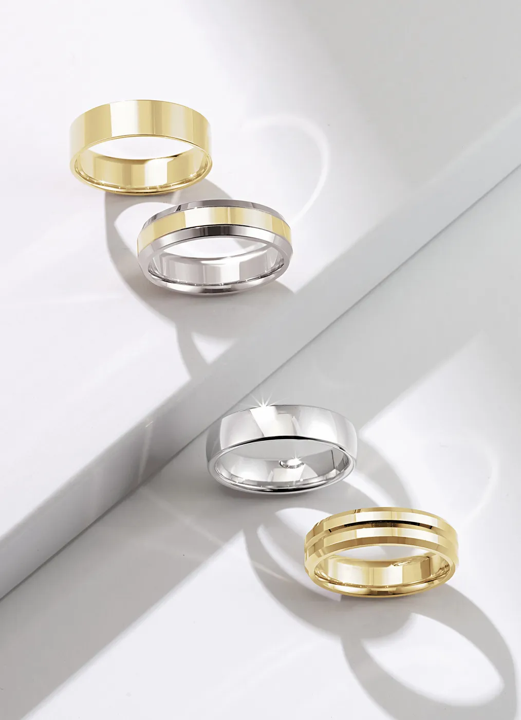 Four gold and silver rings on a white surface with shadows.