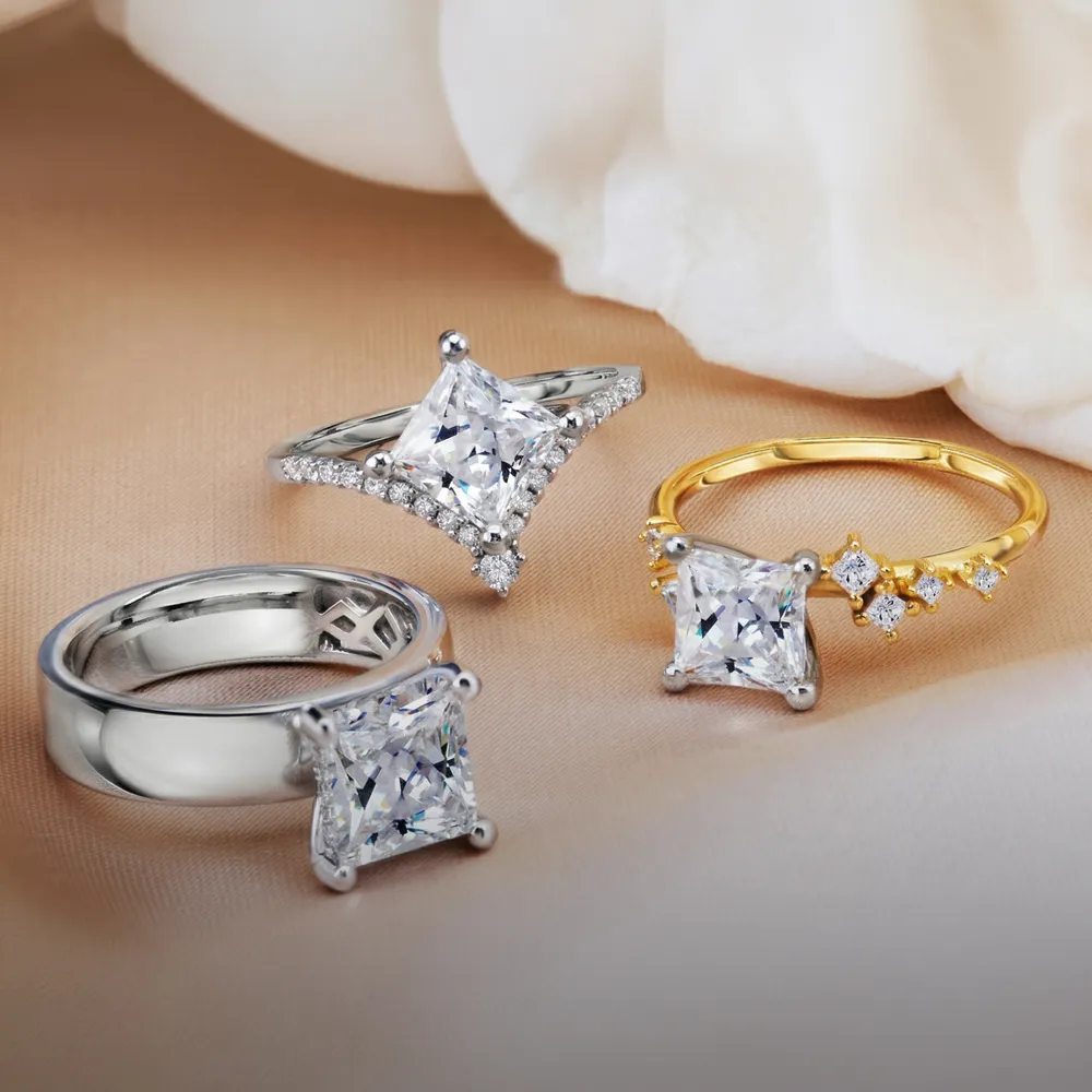 Three elegant engagement rings with large square diamonds on a soft fabric background.