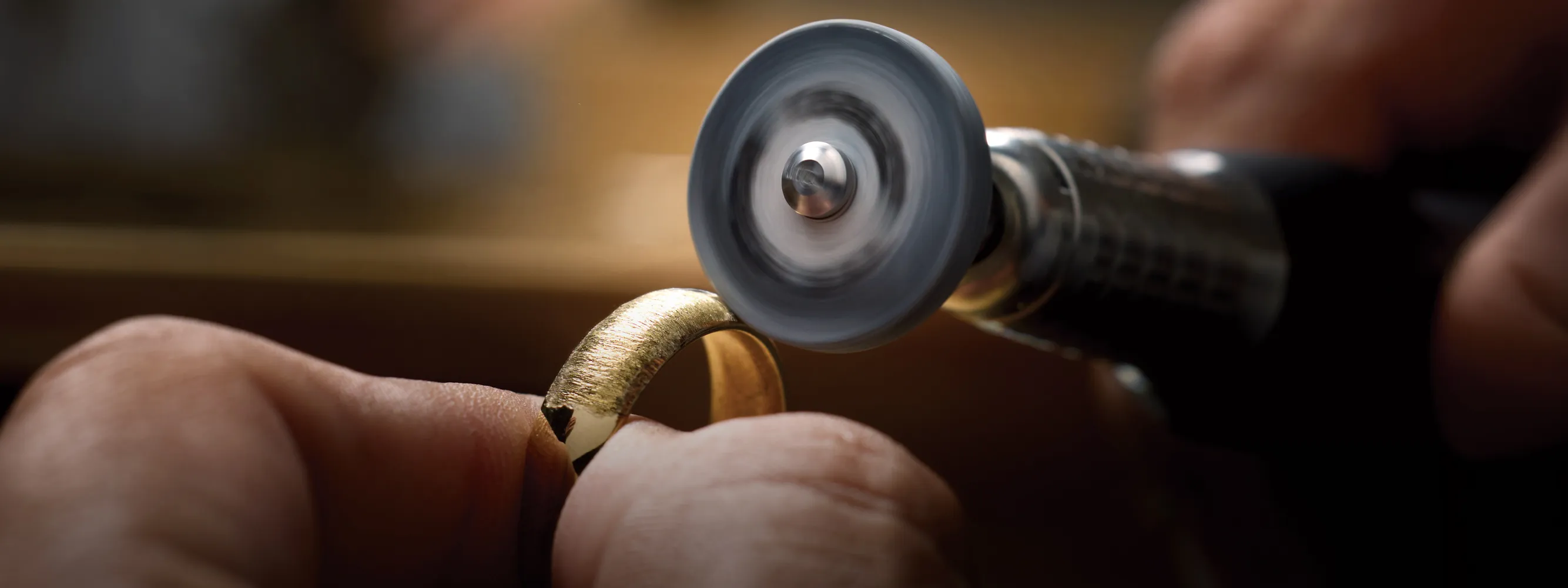 A jeweler polishes a gold ring with a rotary tool. 