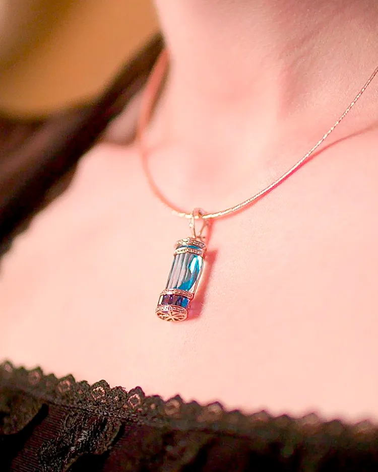 Elegant blue gemstone pendant necklace worn on a delicate chain, showcased on a person's neck.