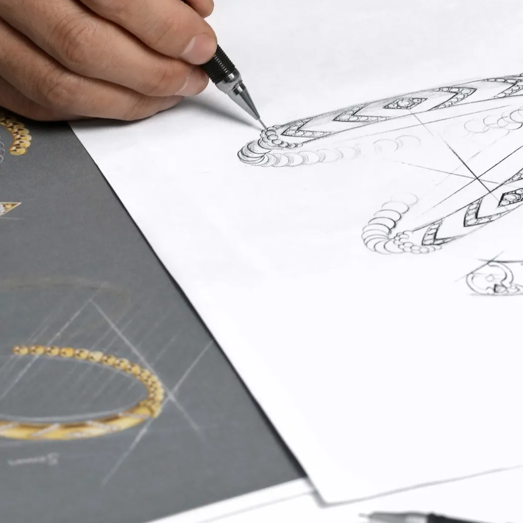 A hand sketches a jewelry design on paper, showcasing intricate details and patterns.