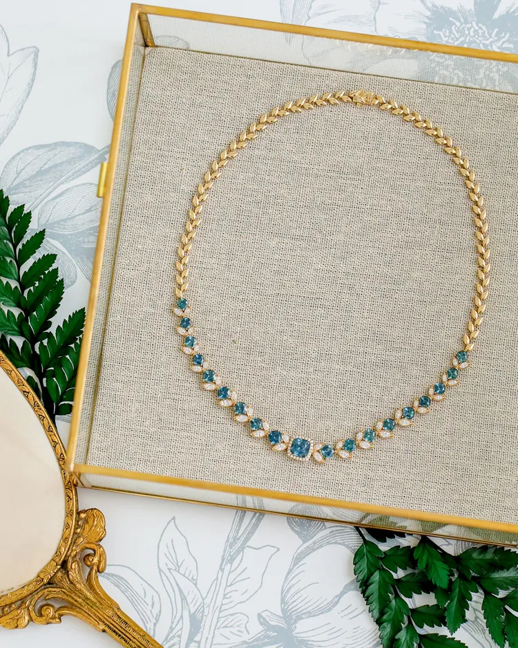 Gold necklace with blue gemstones displayed on a textured background.