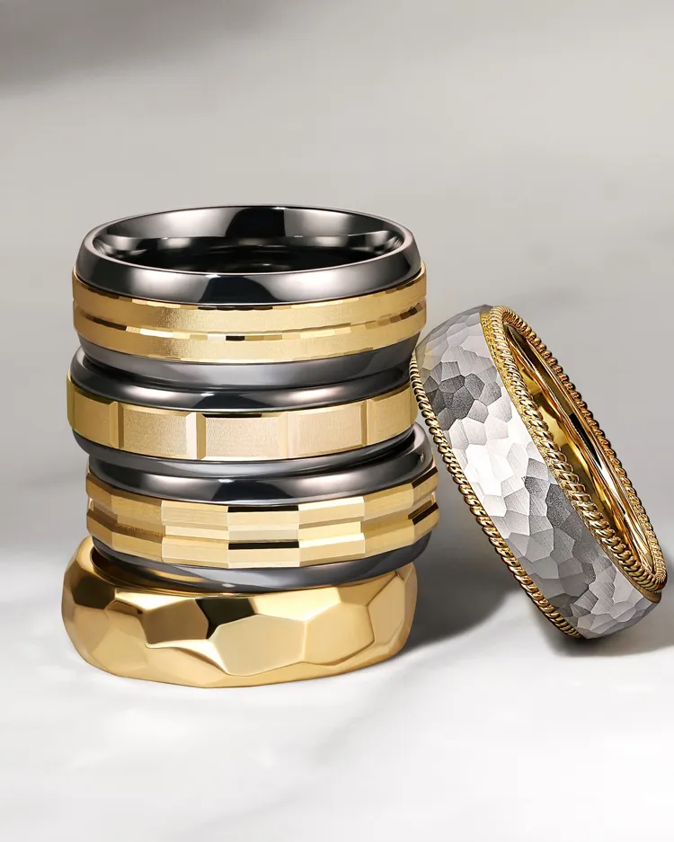 Stack of men's wedding bands in gold and black, showcasing various textures and designs.