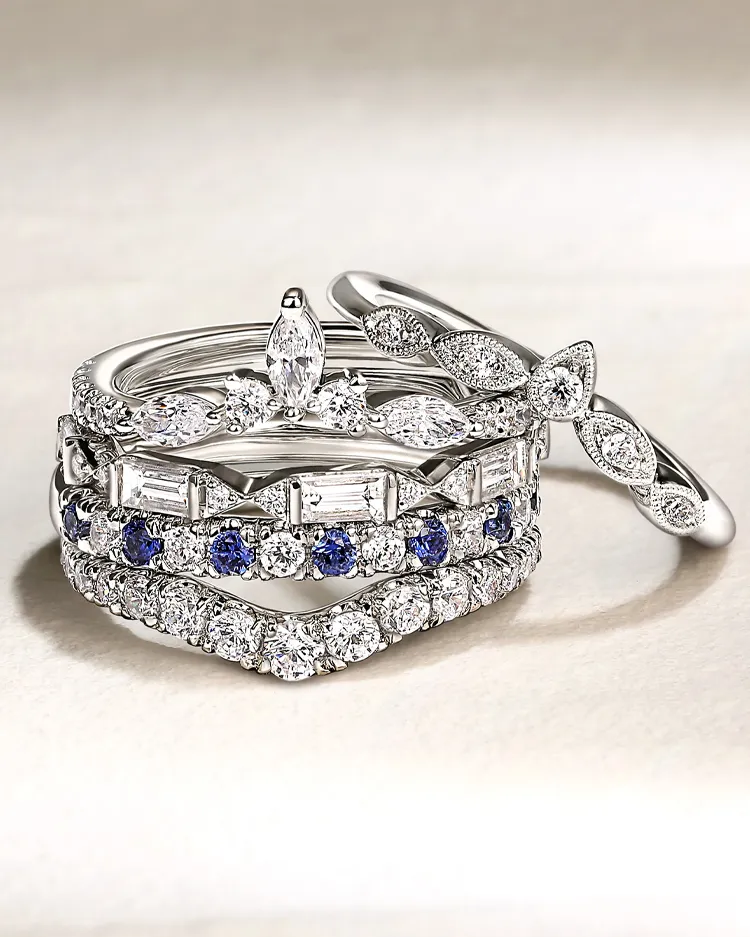 Elegant stack of diamond and sapphire rings displayed on a soft surface, showcasing fine jewelry.