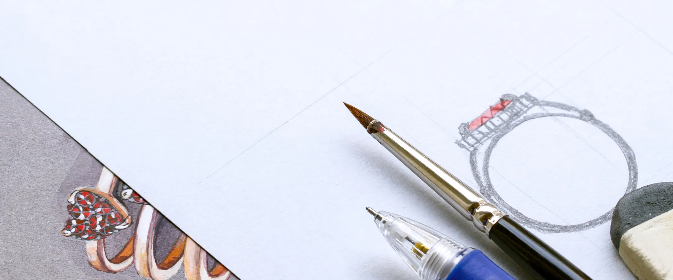 Close-up of a paintbrush and pen beside a ring sketch on paper, inviting you to start a custom jewelry project.