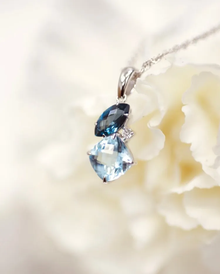 Elegant blue gemstone pendant necklace with silver chain, displayed against a soft floral background.