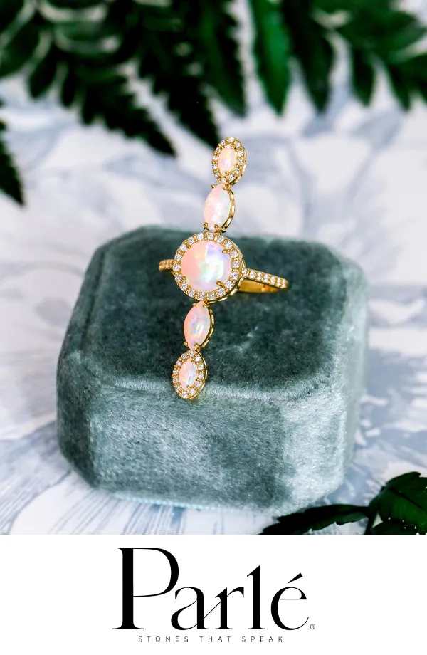 Gold ring with opal stones and diamonds on a gray velvet display.