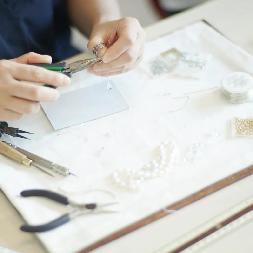 A person using pliers to create jewelry, surrounded by beads and tools on a work surface.