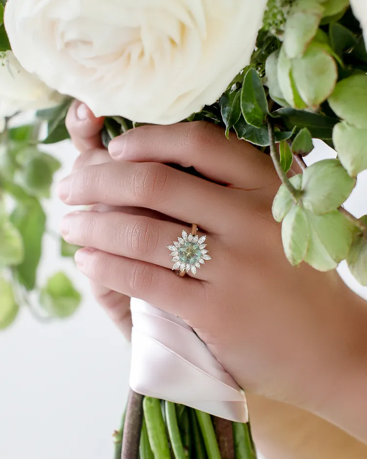A hand holding a bouquet of white roses, showcasing a sparkling floral engagement ring.