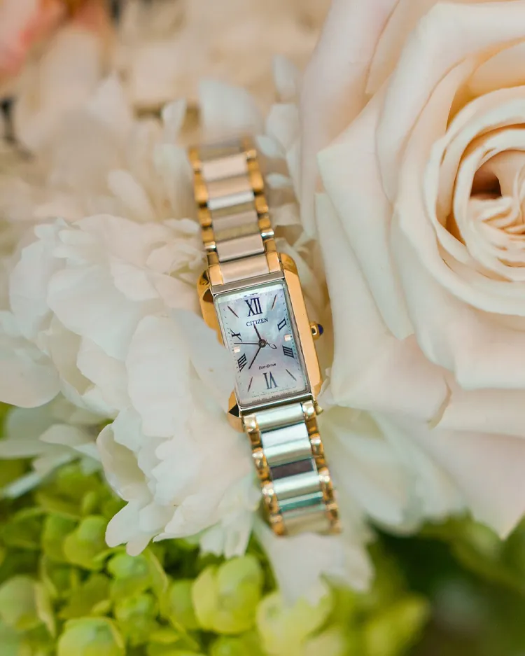 Elegant Citizen watch nestled among white roses and greenery, showcasing fine jewelry.