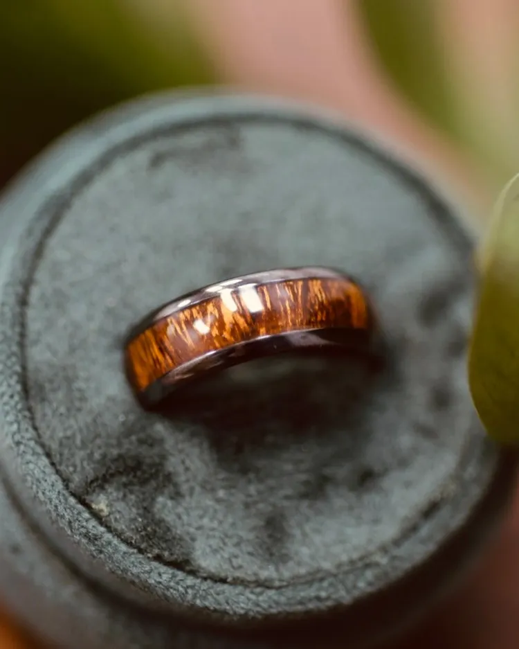 A close-up of a brown and black wedding band displayed on a green velvet cushion.