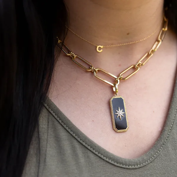 Close-up of layered gold necklaces featuring a black pendant with a star design and a delicate initial charm.