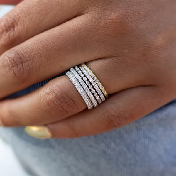 Four elegant diamond wedding bands stacked on a hand, showcasing a mix of white and yellow gold. Visit Sather's Leading Jewelers