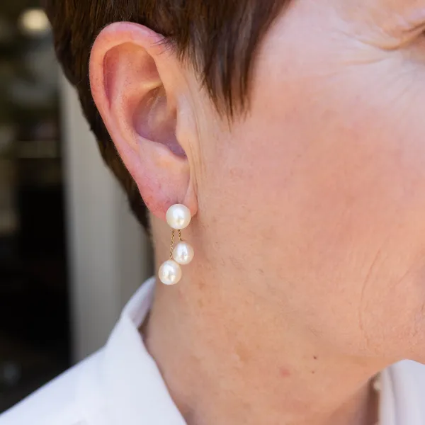Elegant pearl drop earrings worn by a woman, showcasing three pearls on a delicate gold chain.