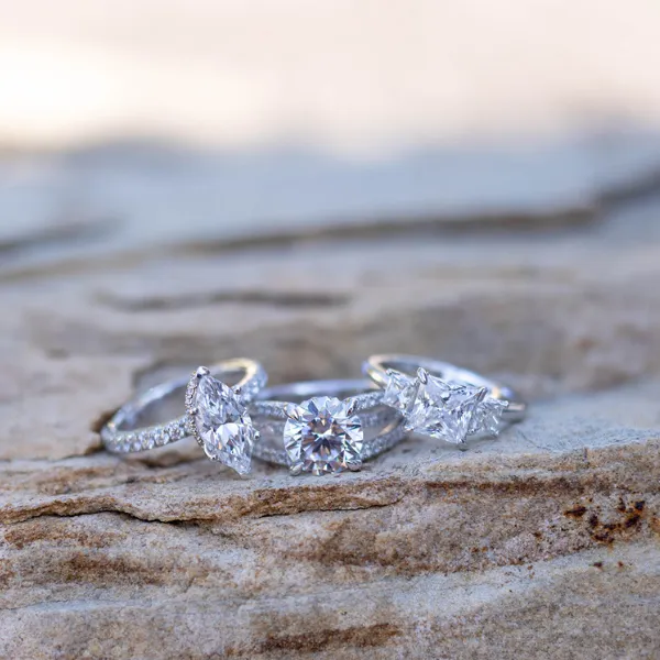 Three elegant diamond engagement rings displayed on a stone surface, showcasing different styles and settings.