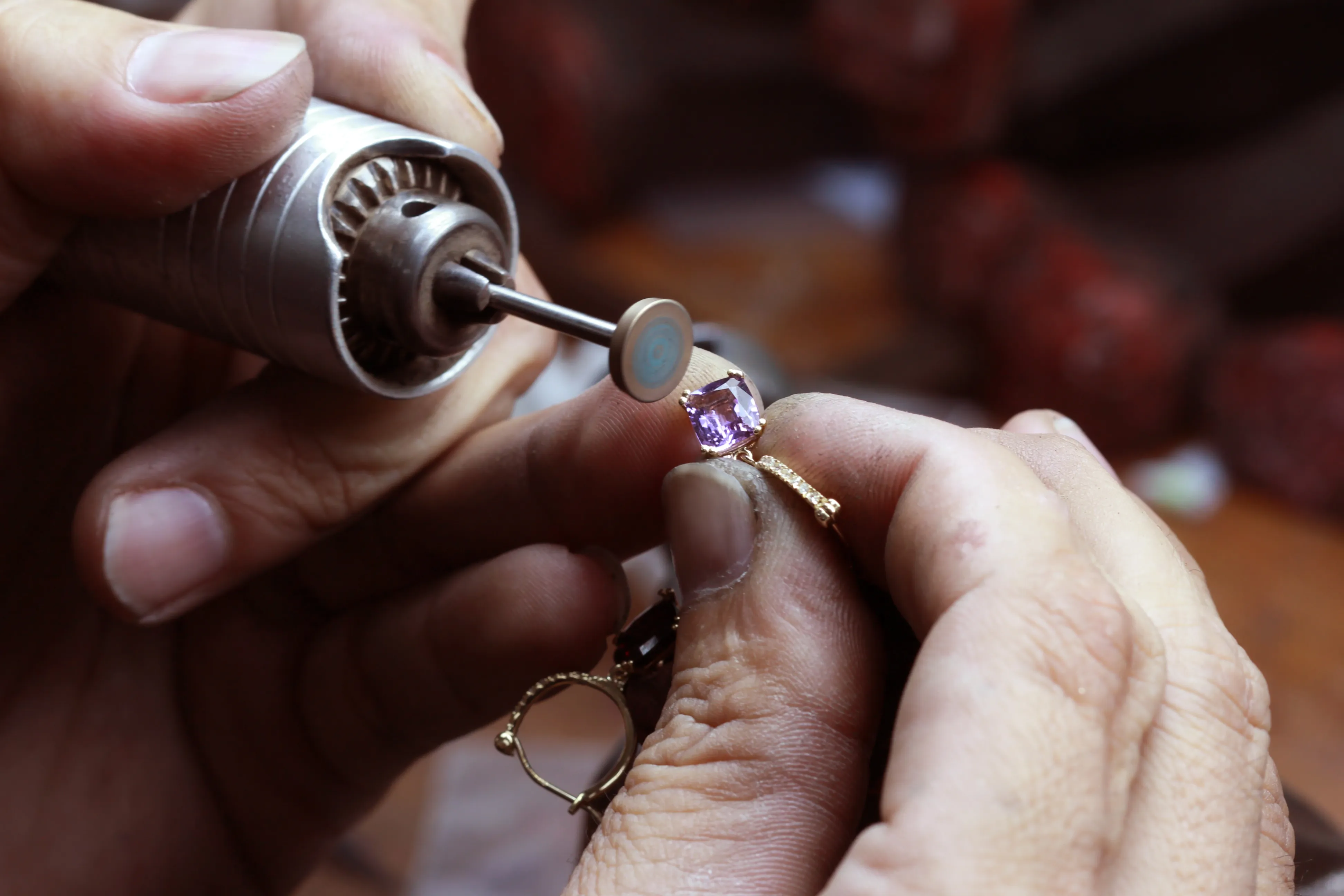 Jeweler using a rotary tool to set a purple gemstone in a gold ring at Sather's Leading Jewelers in Fort Collins. Learn More.