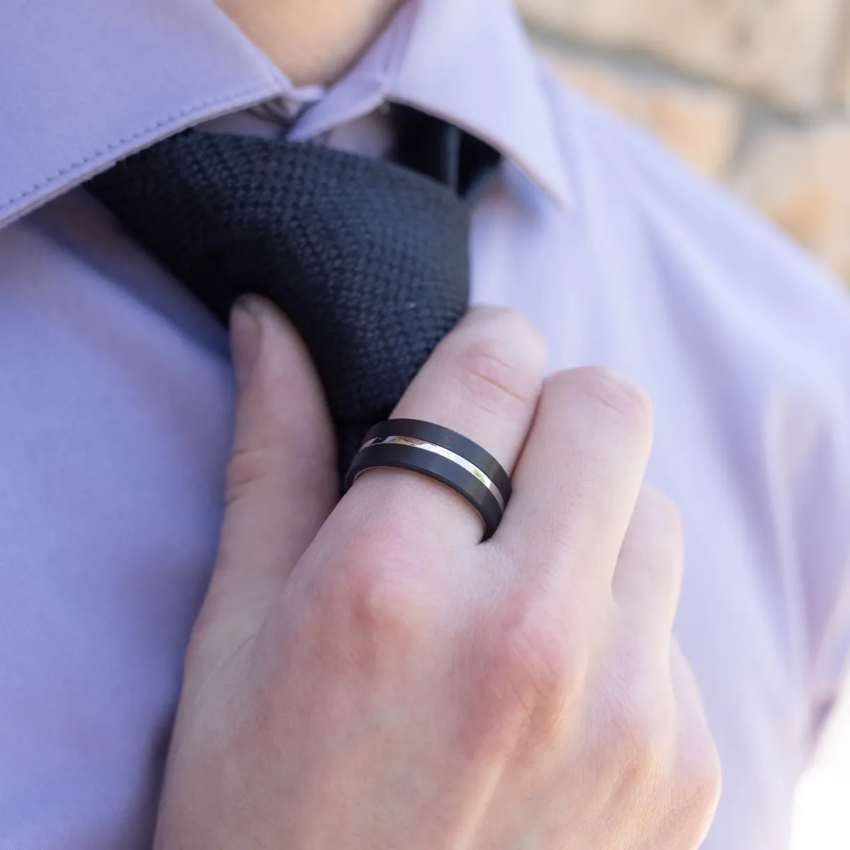 Man in a suit adjusting his tie, wearing a silver wedding band.