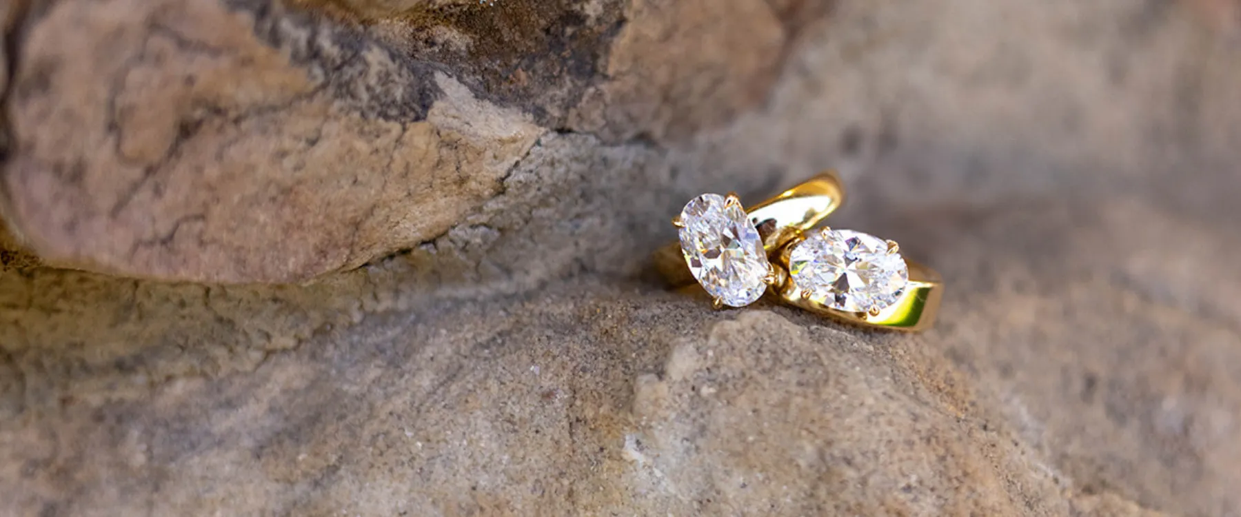 Elegant gold rings with sparkling diamonds resting on a textured stone surface. Click to shop A. Jaffe at Sather's Leading Jewel