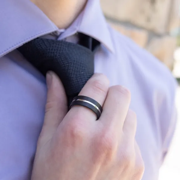 Man adjusting his tie while wearing a black wedding band. Explore men's wedding bands at Sather's Leading Jewelers.
