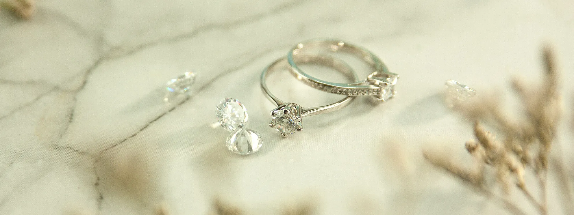 Two elegant diamond rings on a marble surface, surrounded by loose diamonds.