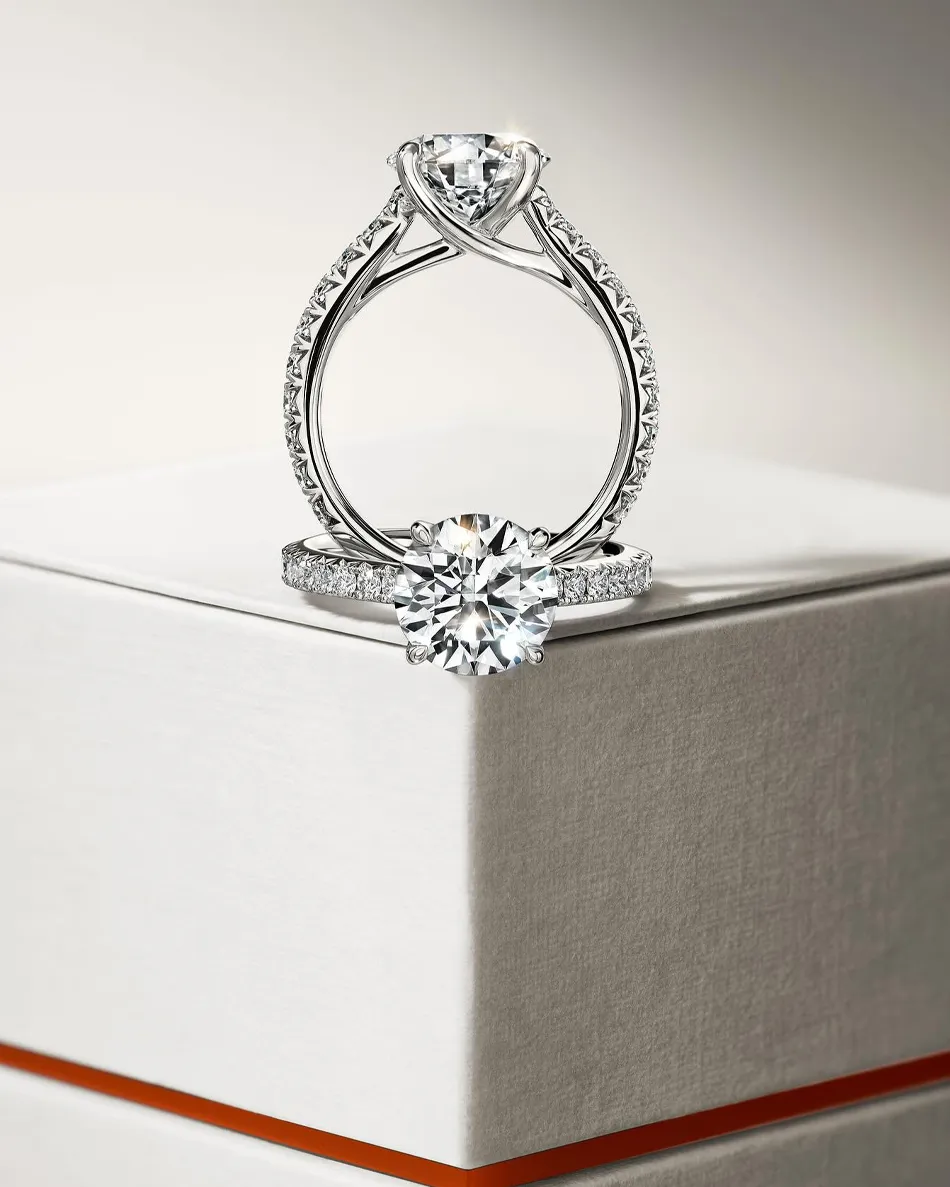 Elegant diamond engagement ring set on a box, featuring a round center stone and intricate band design.