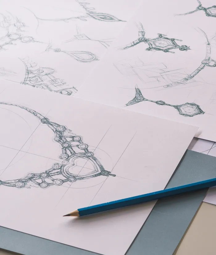 Sketches of intricate jewelry designs on paper with a blue pencil, showcasing custom jewelry concepts.