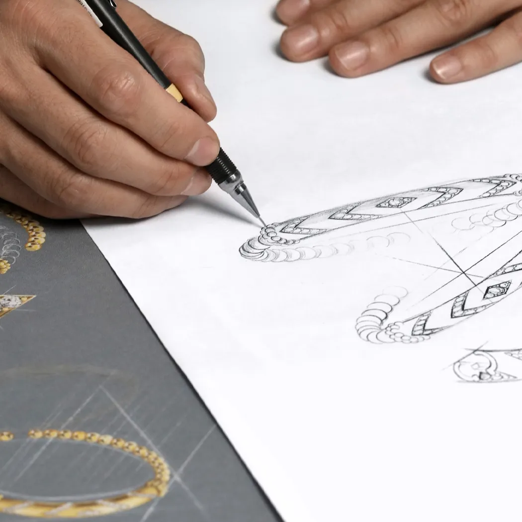 A hand sketches intricate jewelry designs on paper.