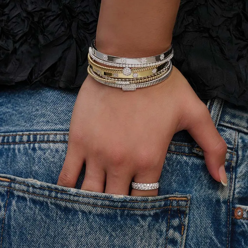 A hand wearing multiple stylish bracelets and a ring, resting in a denim pocket.
