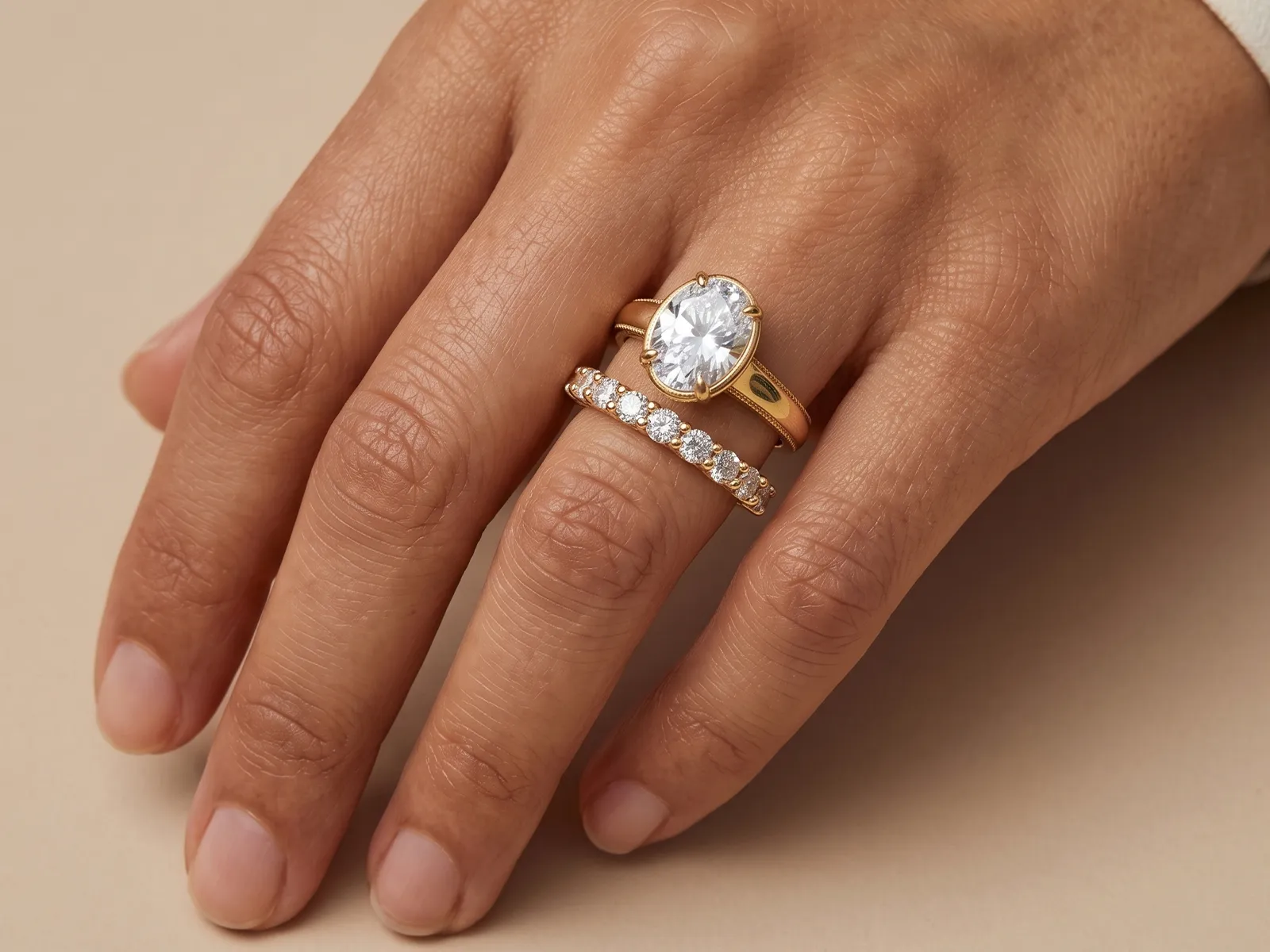 A hand wearing two gold rings with a large oval gemstone and a diamond band.