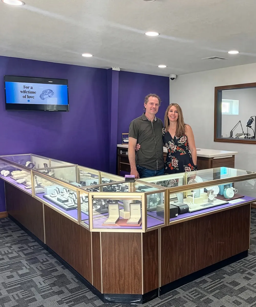 A couple stands in a jewelry store with display cases and a purple wall.