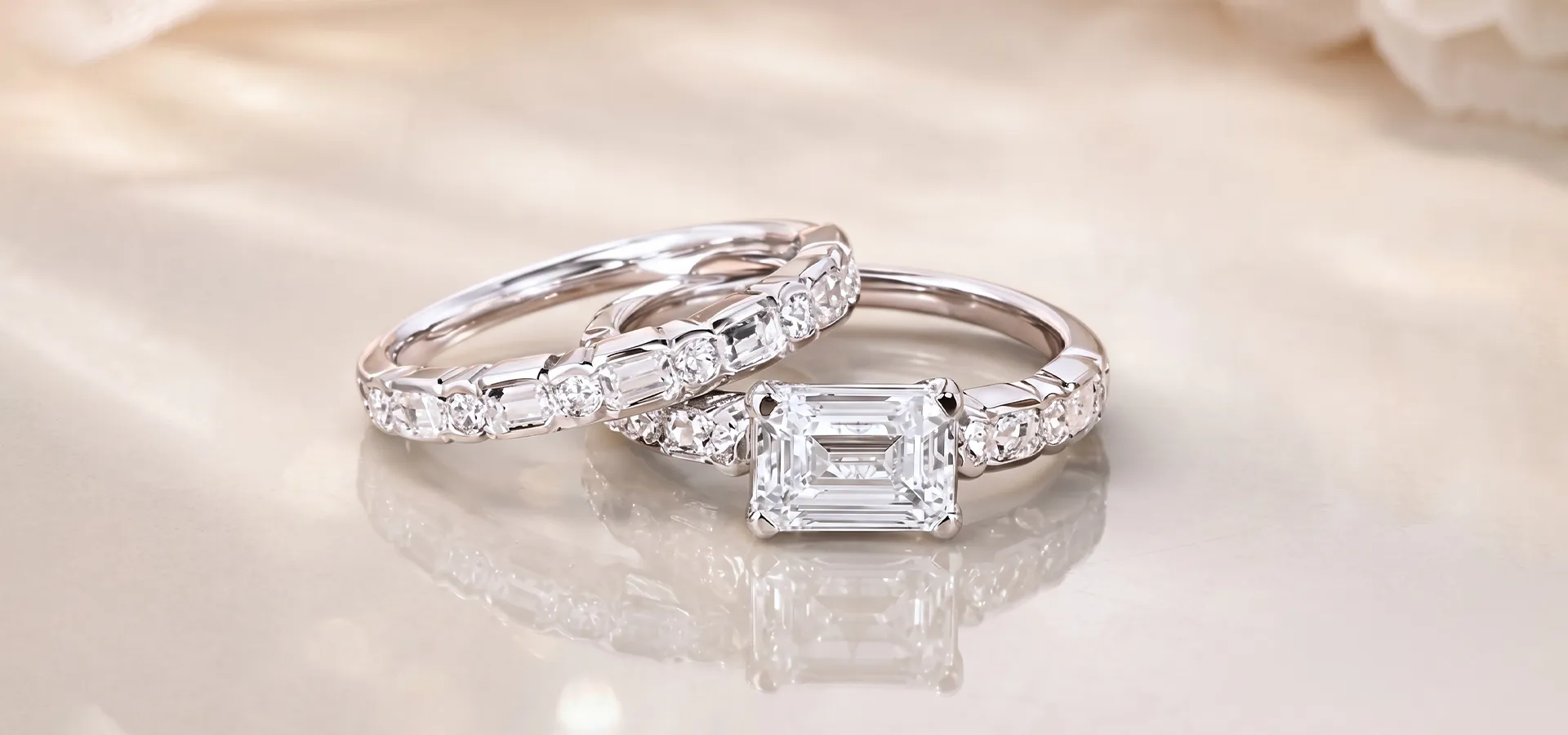 Two diamond rings with emerald and round cuts on a reflective surface.